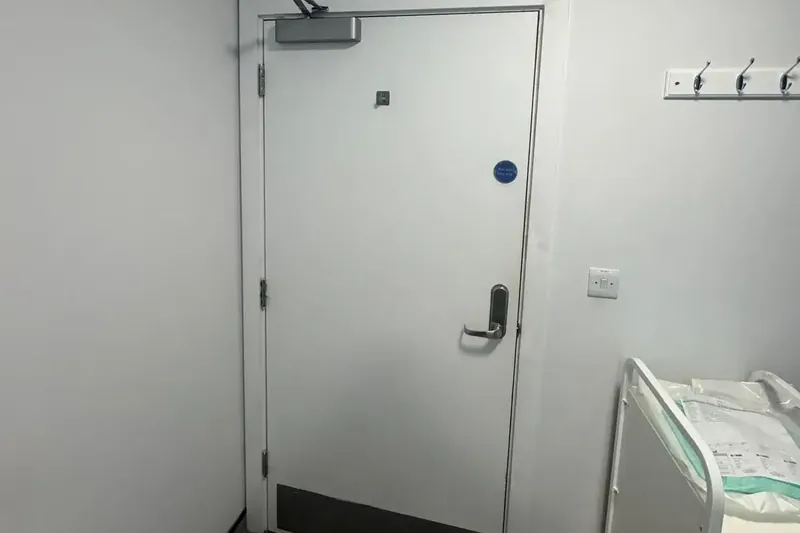 White fire door with overhead closer and keypad lock in a clinical room