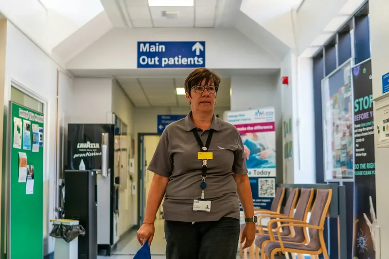 NHS hospital corridor with staff member walking past Main Out Patients signage
